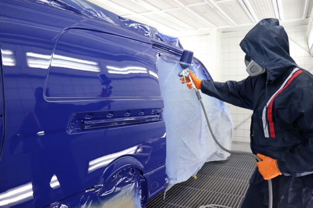 Ein Lackierer sprüht einen Van blau an